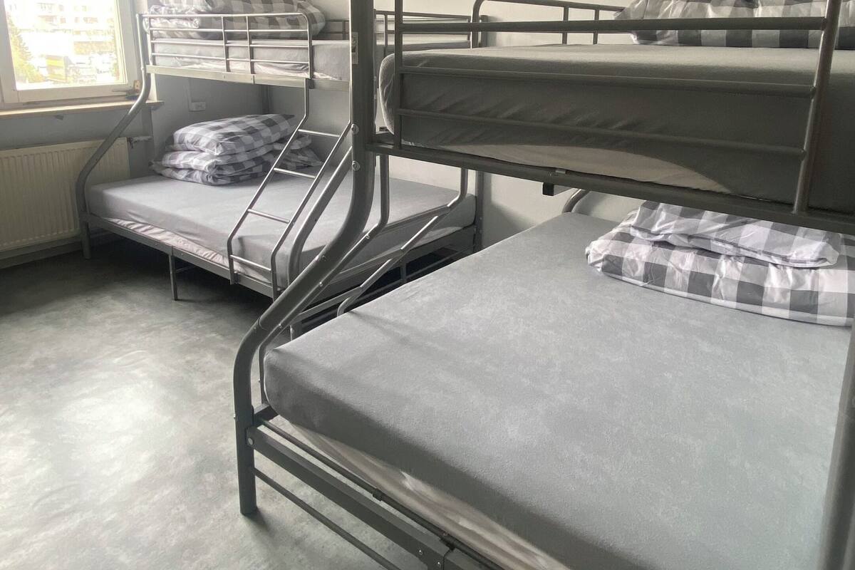 A dormitory room with bunk beds, a window with blinds, and a radiator.