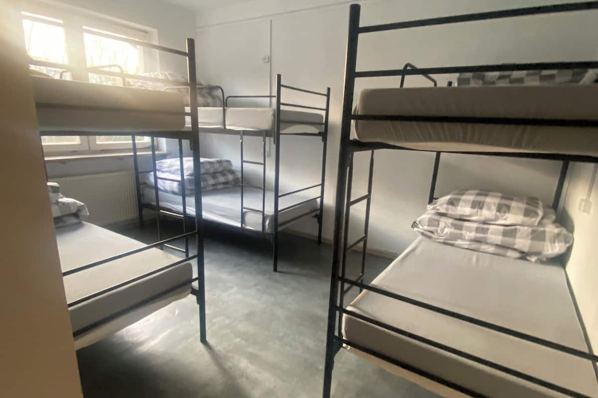 A dormitory room with bunk beds, a radiator, and a window with blinds.