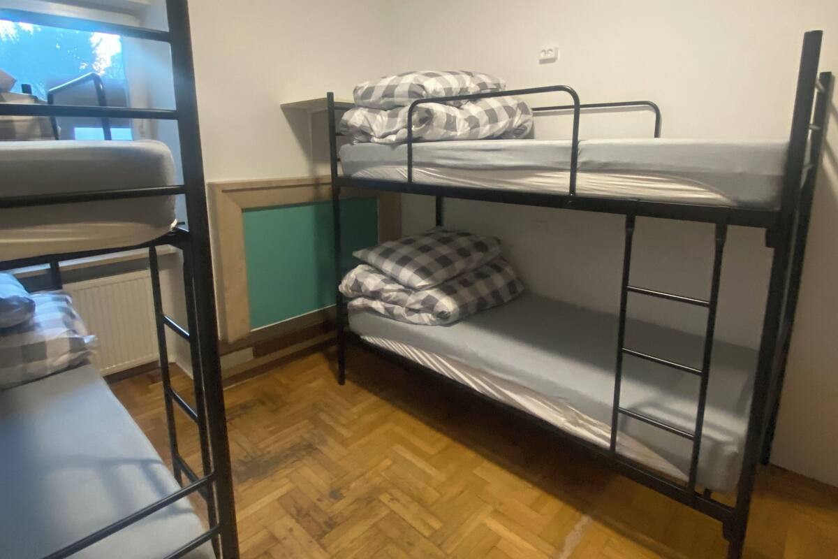 A bunk bed room with a wooden floor, a window with blinds, and a radiator.