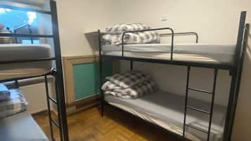 A bunk bed room with a wooden floor, a window with blinds, and a radiator.
