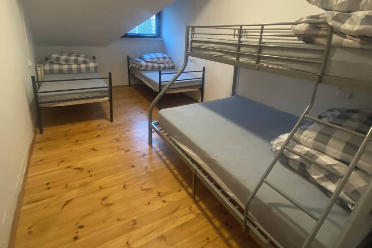 A narrow room with wooden flooring, two bunk beds, a window, and a sloped ceiling.