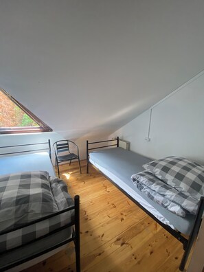 A small, single-room with a sloped ceiling, two metal bunk beds, a wooden floor, a chair, and a window providing natural light. - Hostel Sofiia (Warsaw)