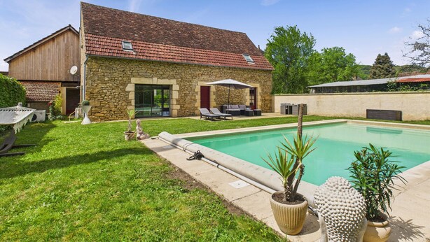 Una casa de piedra con piscina, mobiliario exterior y un césped bien cuidado.