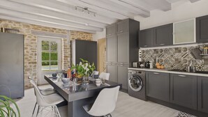 Una cocina moderna con armarios grises, lavadora integrada y una zona de comedor con isla central y dos sillas.