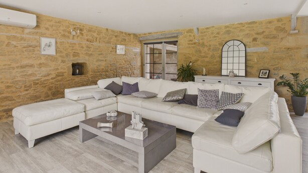 Una sala de estar moderna con una pared de piedra, un conjunto de sofá blanco, una mesa de centro de mármol y un espejo grande.