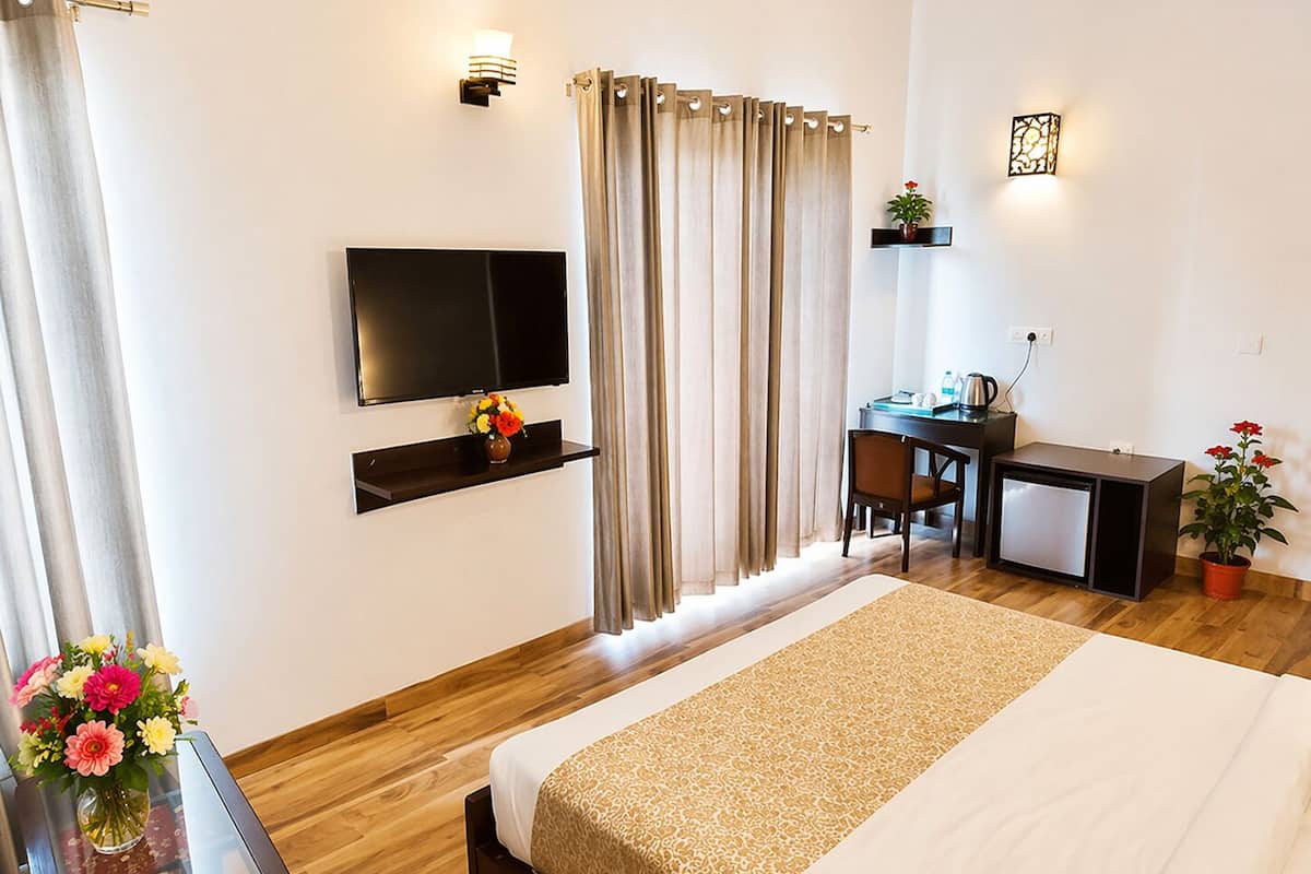 Habitació d'hotel amb llit, televisió, escriptori, cadira i plantes en testos.