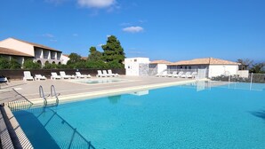 A clear blue pool with a wooden deck and lounge chairs, surrounded by buildings and trees. - T2 renovated chic - terrace & sea view (Linguizzetta)