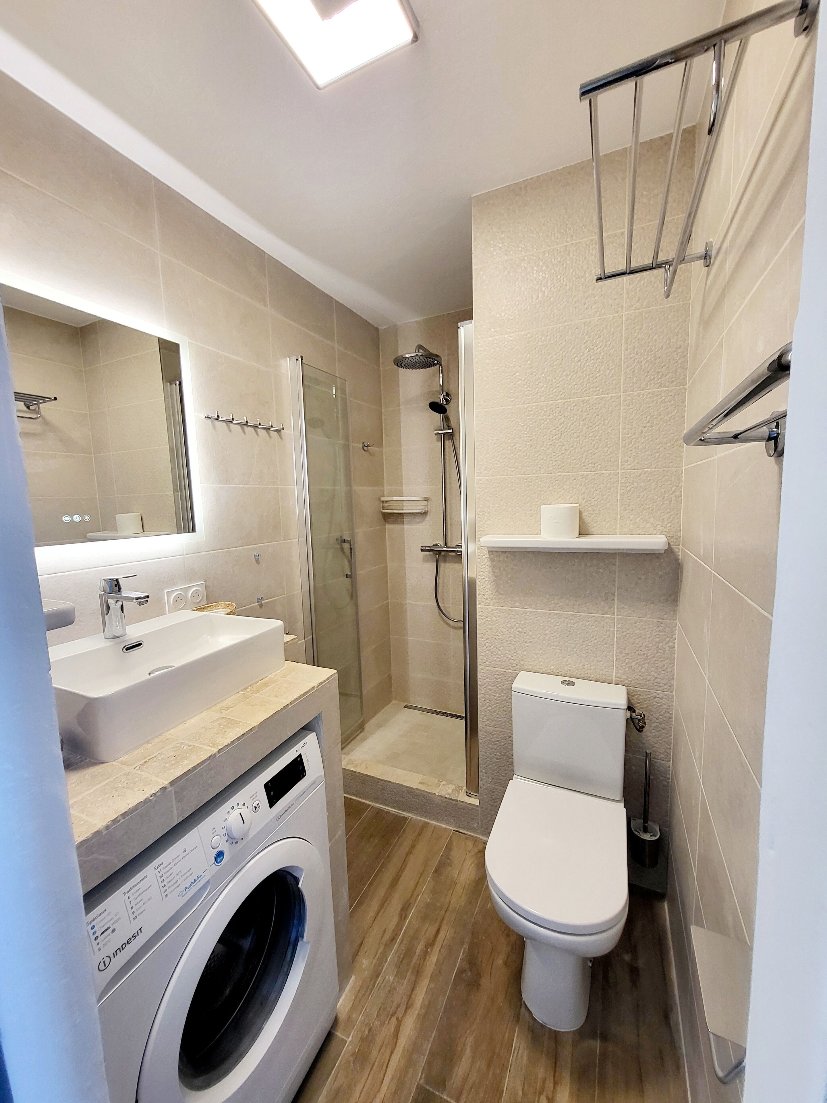 A modern bathroom with a glass-enclosed shower, a built-in washing machine, and a toilet.