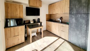 A modern kitchen with wooden cabinets, a black countertop, a built-in microwave, a coffee maker, and a TV mounted on the wall. - T2 renovated chic - terrace & sea view (Linguizzetta)