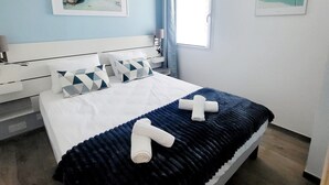 A bedroom with a bed, a nightstand, a lamp, a window, and two framed pictures on the wall. - T2 renovated chic - terrace & sea view (Linguizzetta)