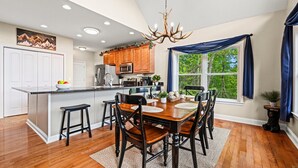 A modern kitchen with wooden cabinets, a central island, and a dining area with a wooden table and chairs. - View-Tastic in The Valley / Hot Tub / Views (Maggie Valley)