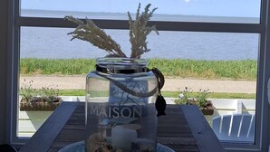 Blick durch ein Fenster, auf einem Tisch steht ein Glas mit dem Aufkleber 'MAISON', eine hängende Dekoration und ein Smartphone.
