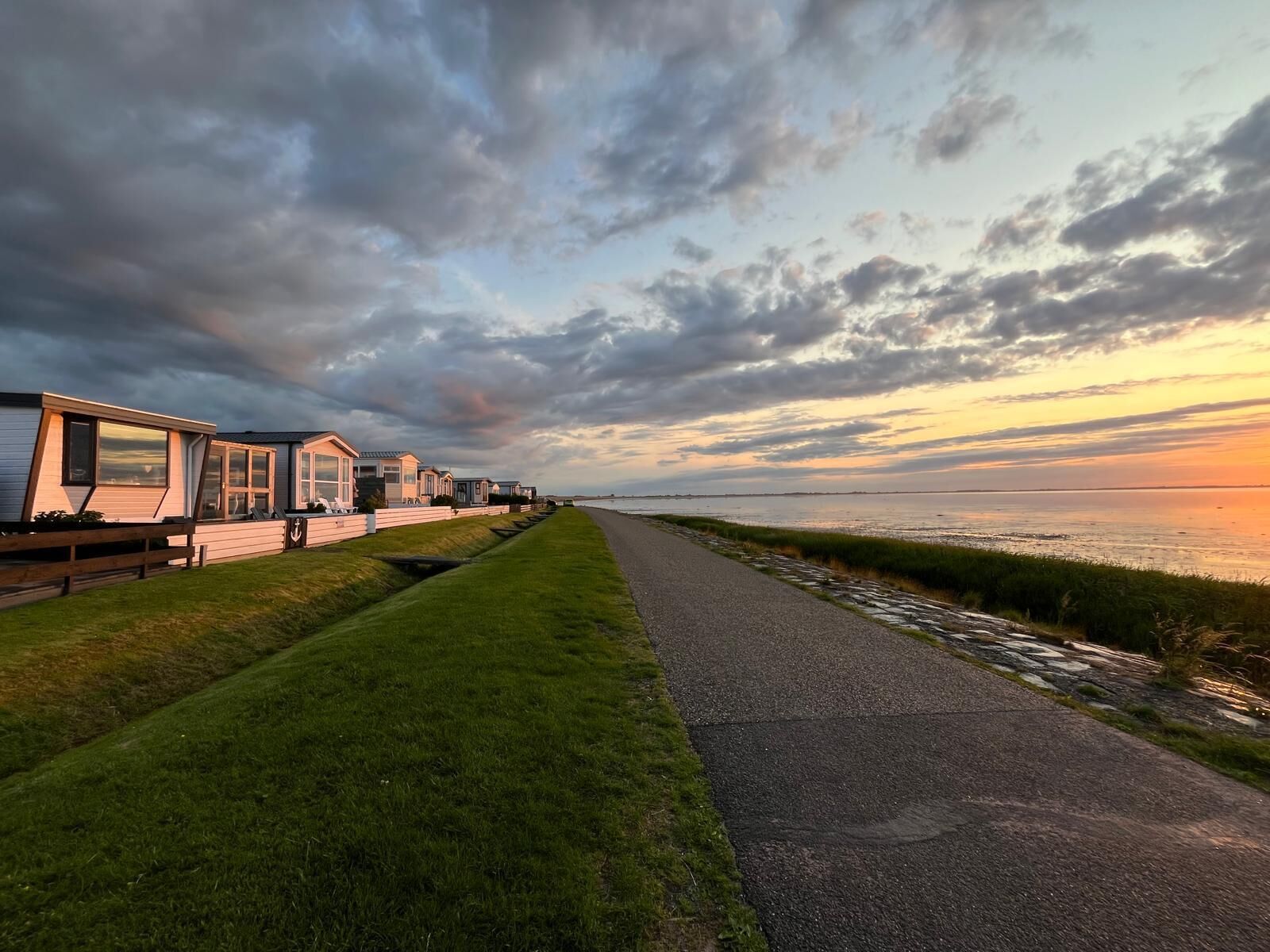Een rij moderne strandbungalows met een verharde looppad en gazon.