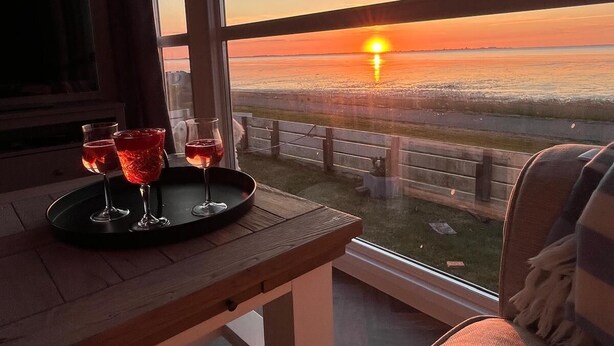 Ein Balkon mit Tisch, gedeckt für Getränke, mit Blick auf einen Sonnenuntergang über dem Wasser.