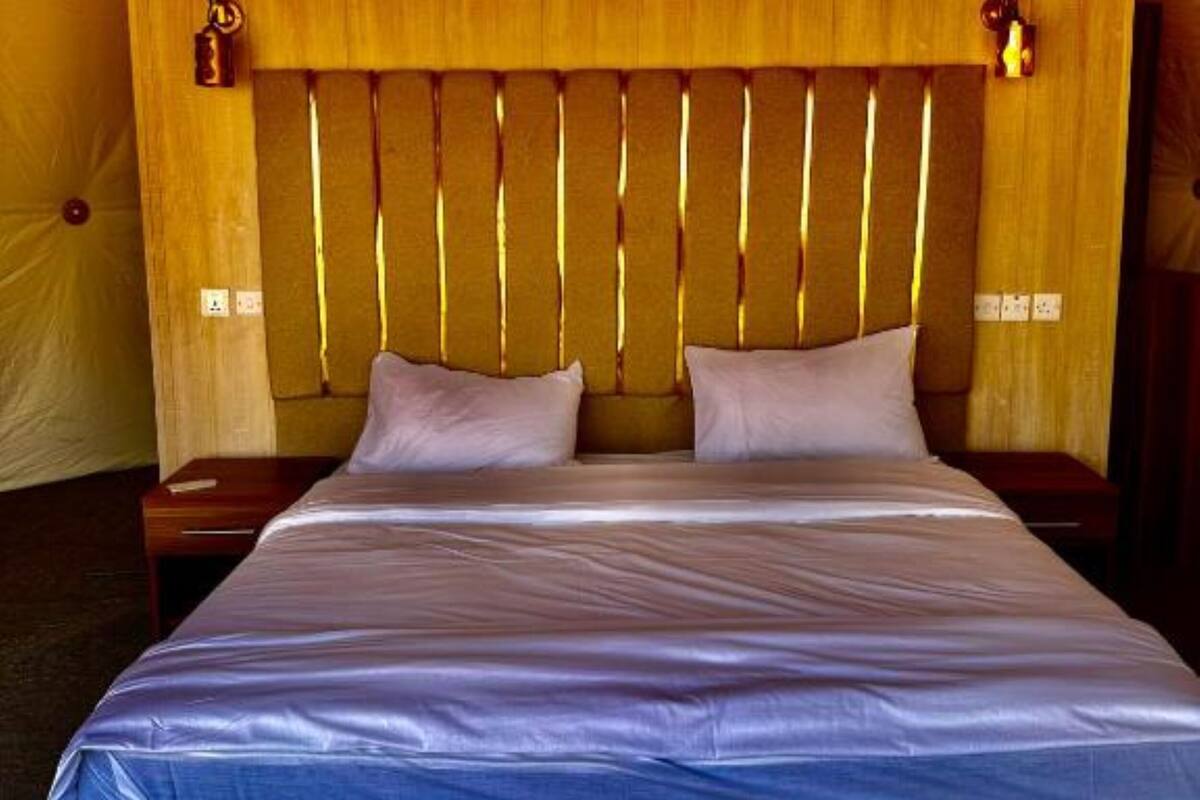 A bed with a wooden headboard, two pillows, and a blue bedspread in a tent-like room.