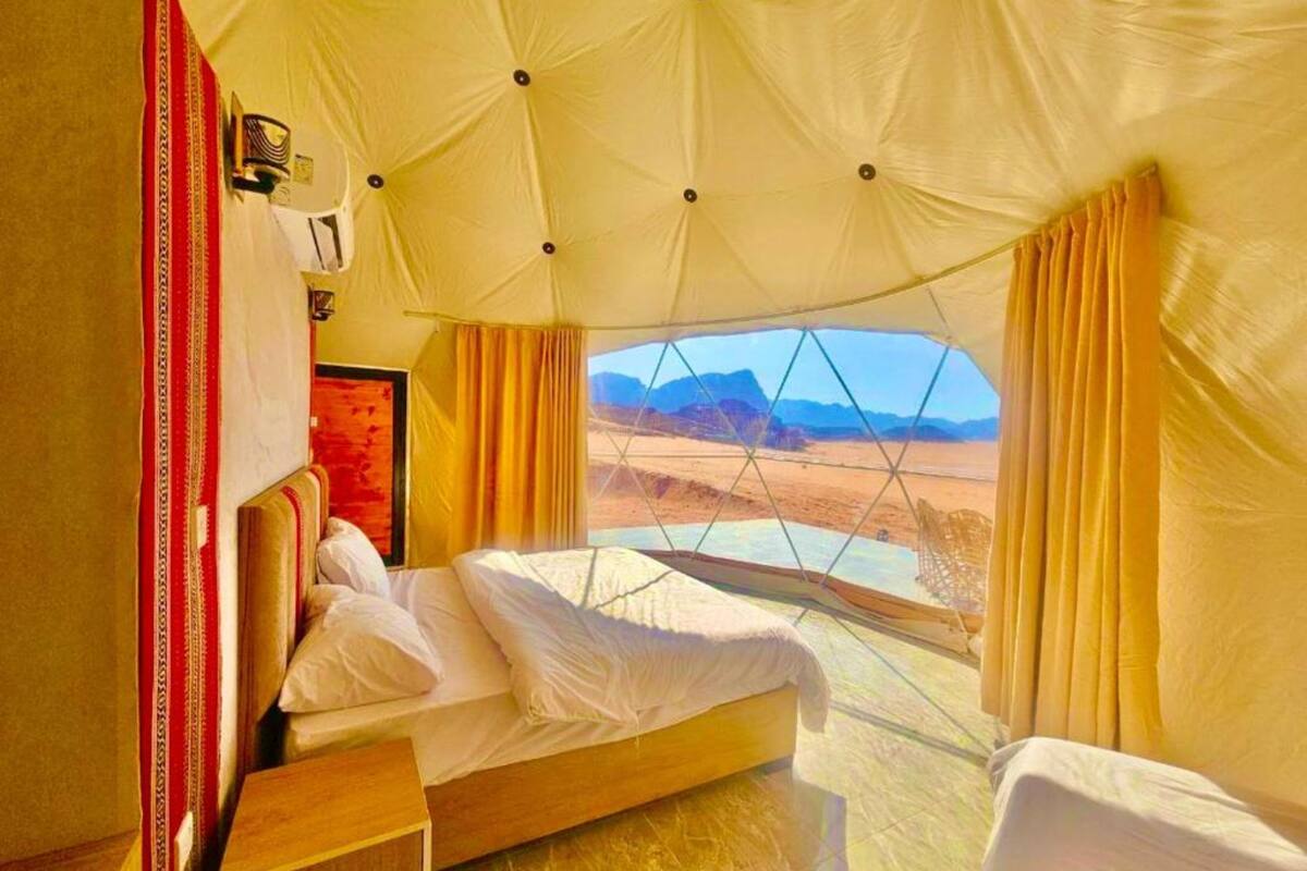 A tent-style room with a bed, a wooden nightstand, and a view of a desert landscape.