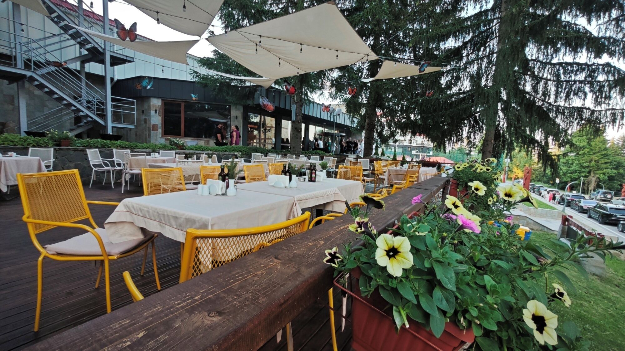 An outdoor dining area with tables and chairs, a wooden deck, and potted plants with flowers.