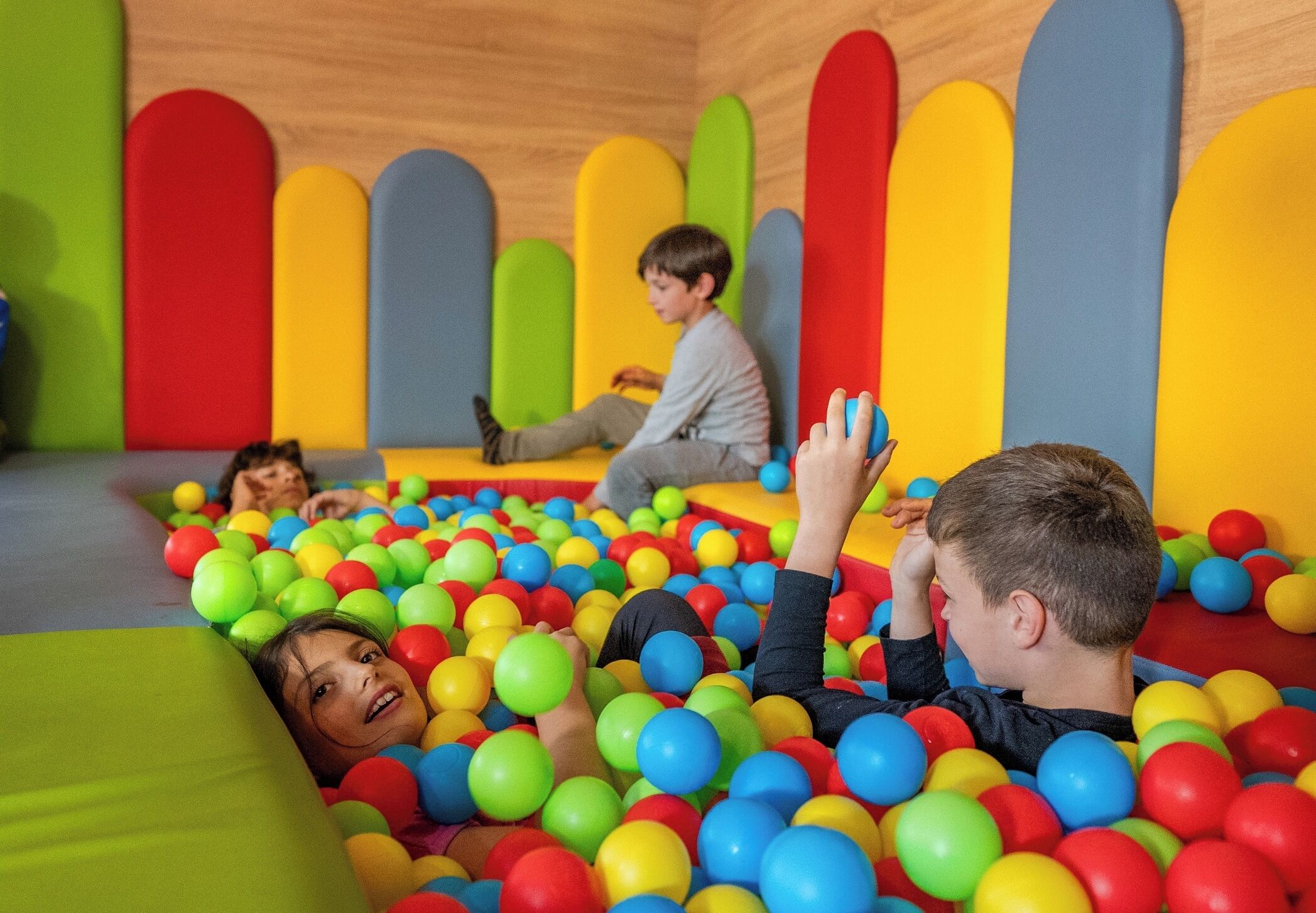 Children playing in a ball pit with colorful foam walls.