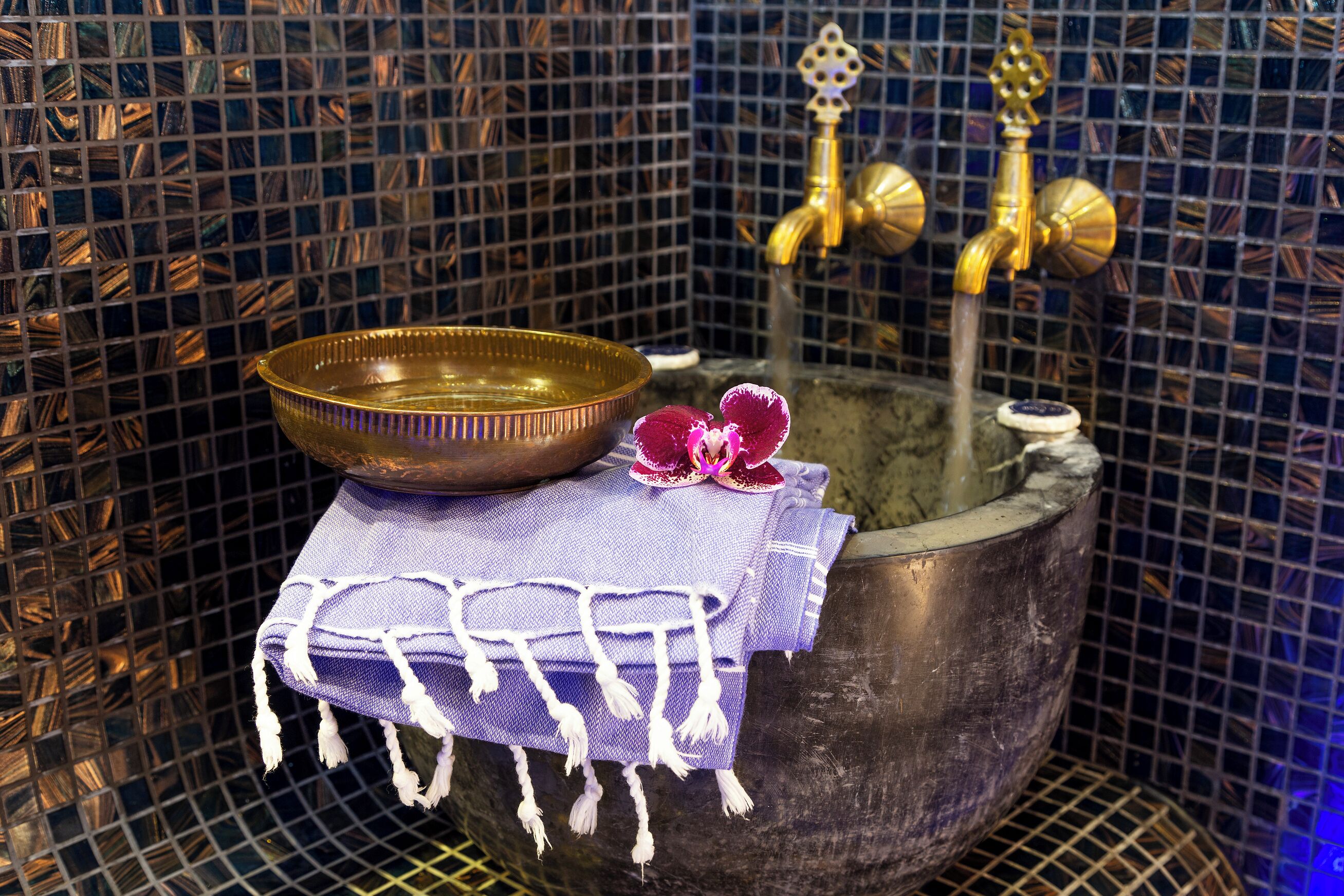 A bathroom with a metal basin, a purple cloth, and a decorative flower.