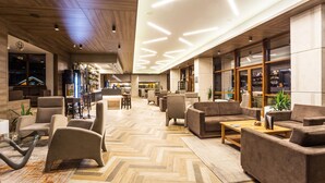 A spacious lobby with modern furniture, a bar area, and a view of the cityscape through large windows. - Perelik hotel  (Pamporovo)