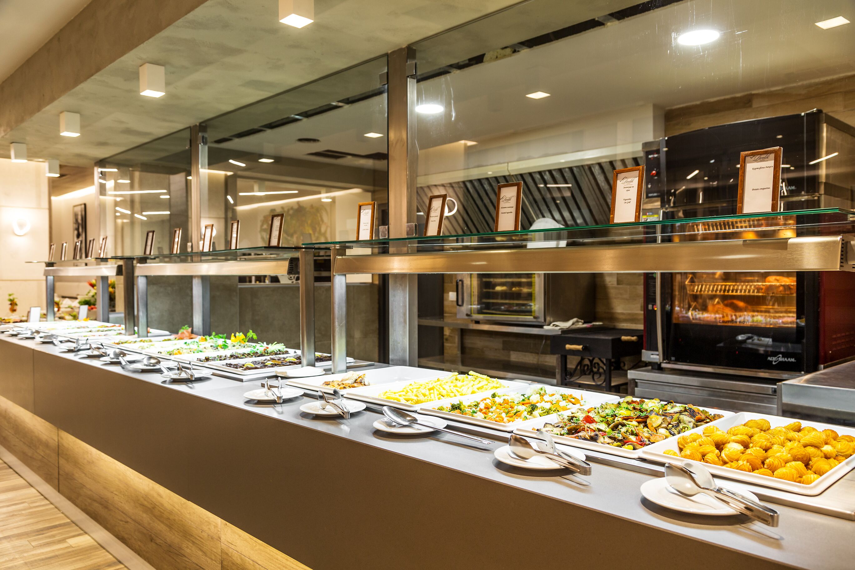 A buffet with various food options, a glass display case, and a kitchen area in the background.