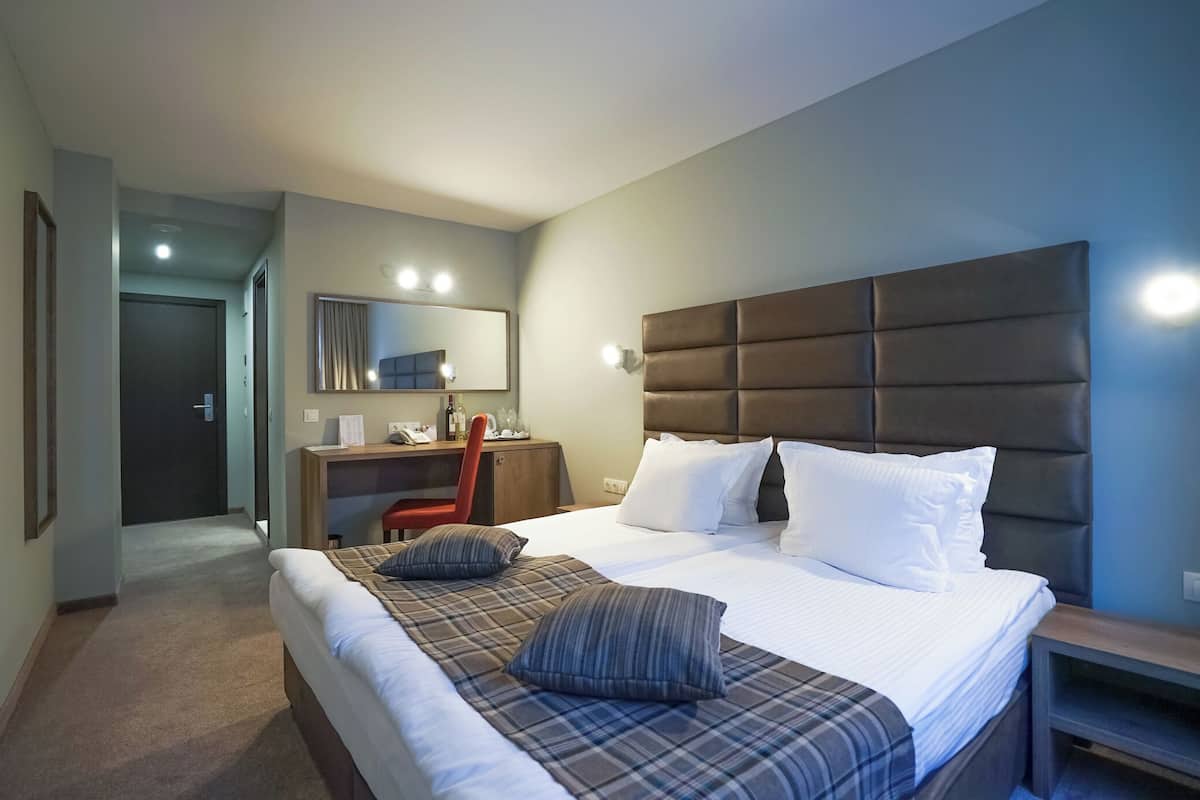 A hotel room with a large bed, a desk with a chair, a mirror, and a headboard.