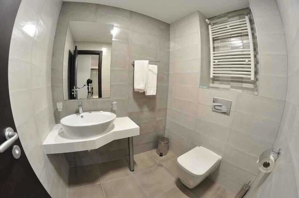 A modern bathroom with a white sink, toilet, and a window with blinds.