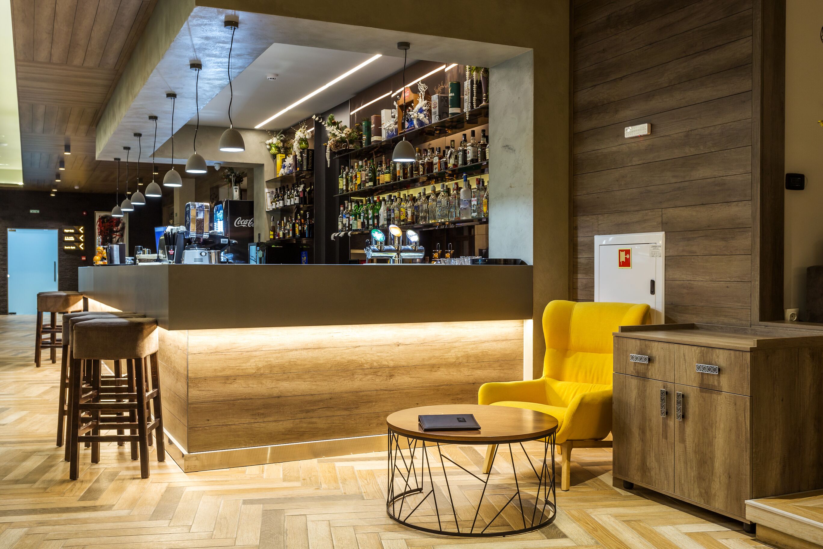 Zona de bar con mostrador de madera, taburetes y un sillón amarillo.