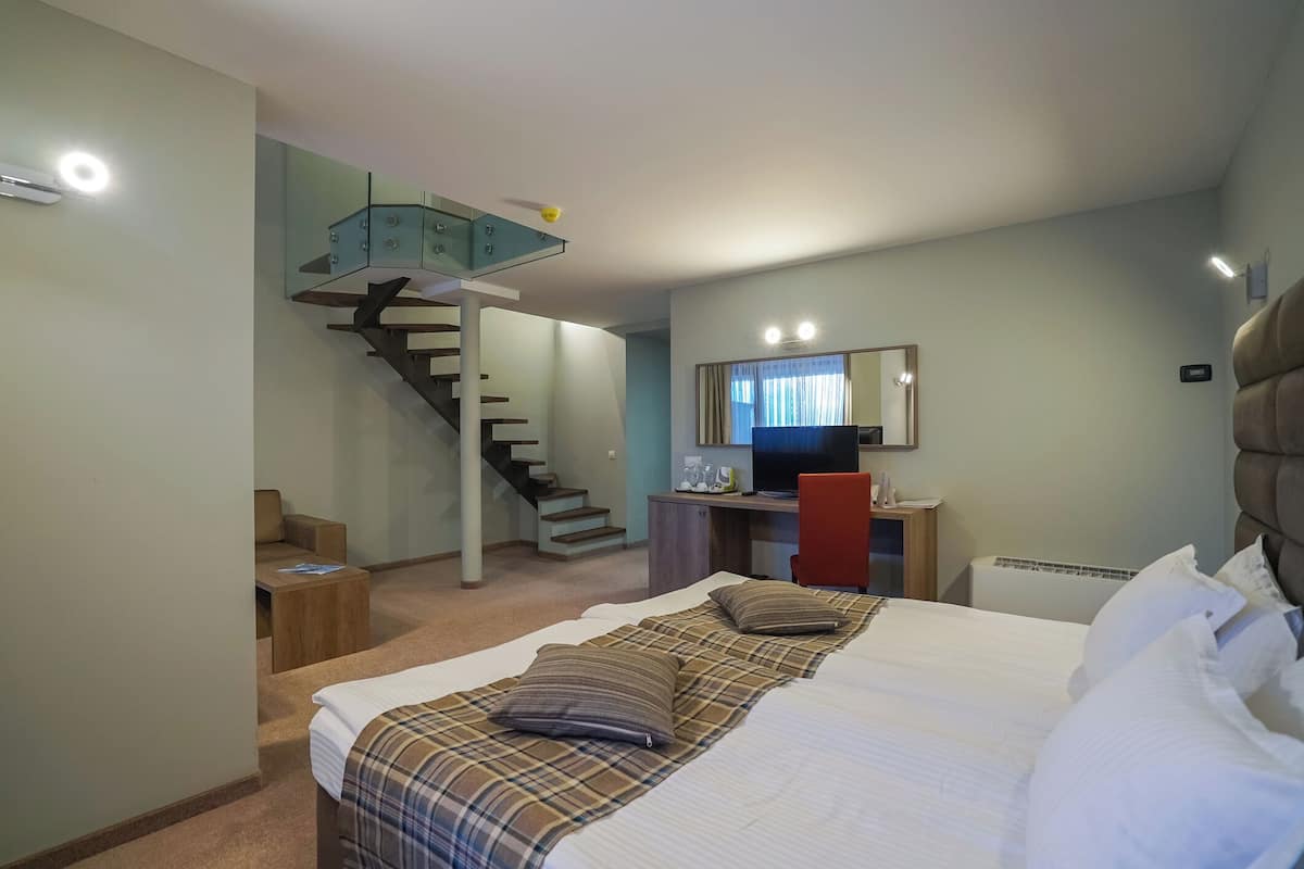 A bedroom with a bed, a desk, a chair, a television, and a staircase.