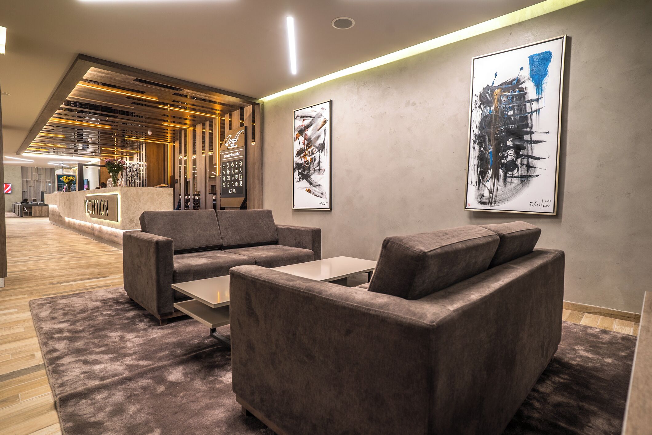 A modern lobby with a reception desk, grey sofas, and abstract art on the walls.