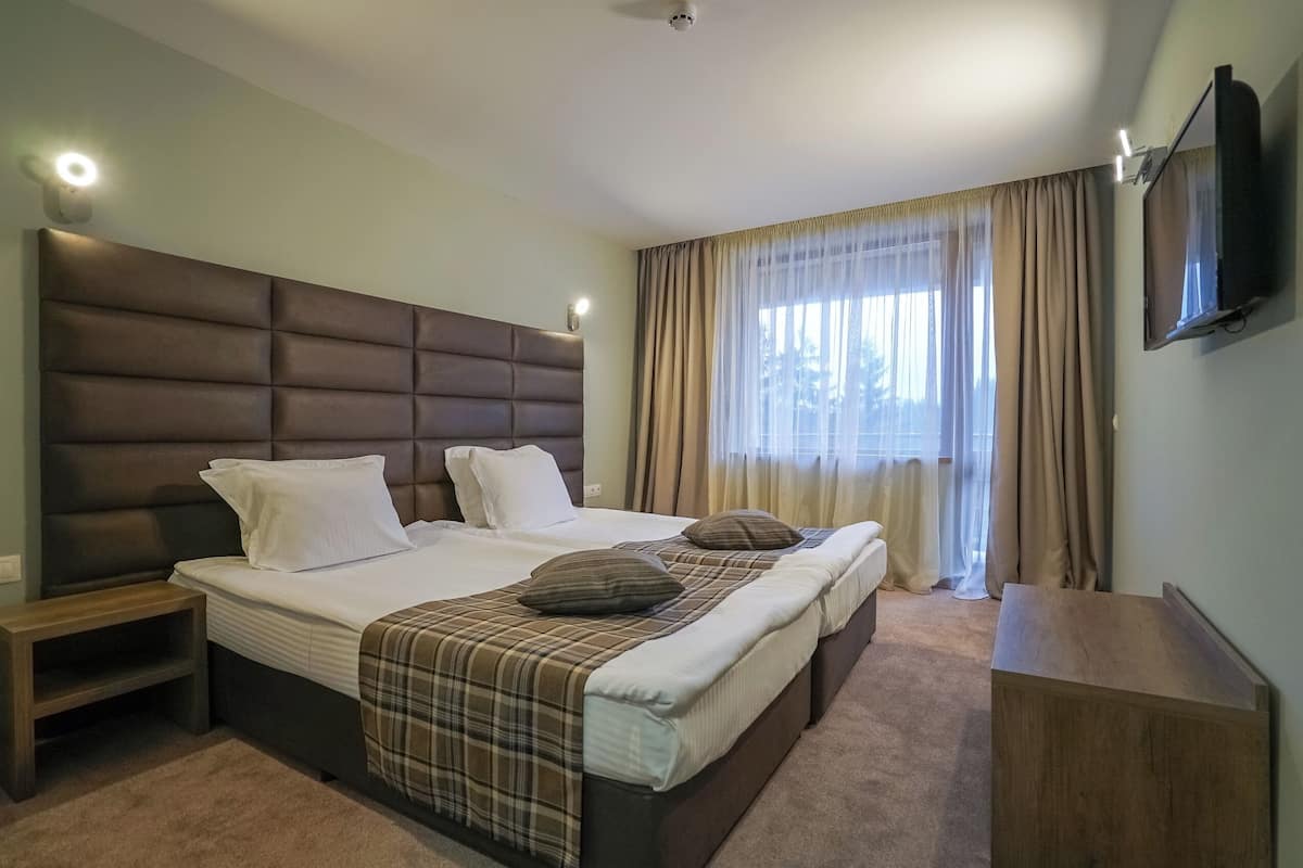 A hotel room with a large bed, a TV mounted on the wall, and a window with curtains.