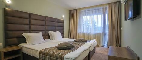 A hotel room with a large bed, a TV mounted on the wall, and a window with curtains.