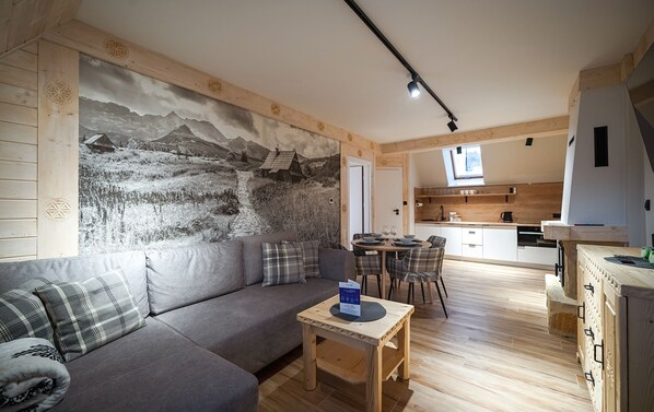 A modern living room with a gray sofa, a small wooden table, and a kitchen in the background. - Apartamenty Sun & Snow Pod Blachówką (Koscielisko)