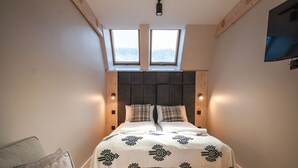 Quarto com uma cama grande, duas claraboias, TV na parede e cabeceira de madeira.