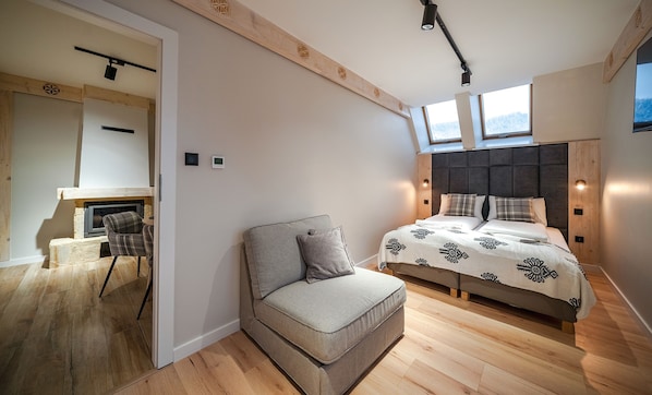 A modern bedroom with a sofa, a bed with patterned bedding, a fireplace, and a large window.