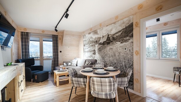 Interior acolhedor de uma cabana, com área de jantar, um sofá e vista para uma paisagem nevada pelas janelas.