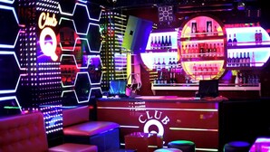 Zona de bar con letreros de neón, una barra y asientos.