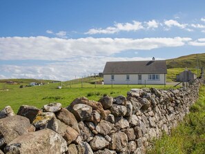 Situated on a grassy hill, this house offers a serene rural setting with a traditional stone wall and a two-story design.