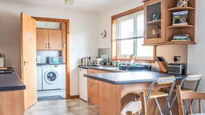 Une cuisine compacte équipée d’un lave-linge, d’un évier et d’un coin repas avec une table et des chaises.