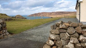 Un sentier côtier menant à un bâtiment d’où l’on peut admirer la mer et les collines.