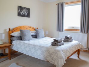 A neatly made bed with pillows, a bedside lamp, and a rolled towel on the floor.