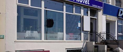 Hotel en primera línea de playa, con un llamativo letrero azul, amplias ventanas y fachada blanca.