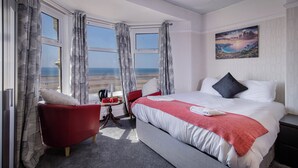 Een hotelkamer met een groot bed, een rode fauteuil, een tafeltje met een lamp en een schilderij aan de muur.