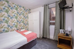 A bedroom with a bed, a wardrobe, a small table with a kettle, and a television on a stand.