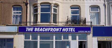 Un immeuble d’angle avec une enseigne indiquant « The Beachfront Hotel », doté d’une grande fenêtre, d’un balcon et d’un escalier menant à l’entrée.