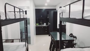 A dormitory room with bunk beds, a small kitchenette, and a glass table.