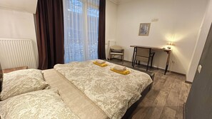 Habitación de hotel con dos camas, un escritorio, una silla y una ventana con cortinas.