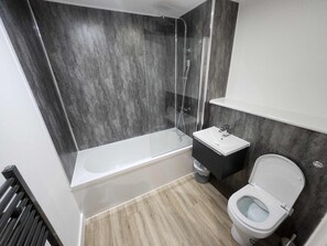 Une salle de bain moderne avec une douche à l’italienne en verre, une baignoire blanche, un meuble-lavabo noir et des toilettes blanches.