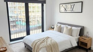 Une chambre moderne avec un grand lit, une table de chevet en bois, une lampe de chevet, un luminaire suspendu et une vue sur l’extérieur grâce à une porte-fenêtre coulissante.