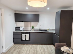 A modern kitchen with dark cabinetry, a microwave, a sink, and a dining area with a glass table and chairs.